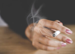 main de femme tenant une cigarette allumée avec de la fumée