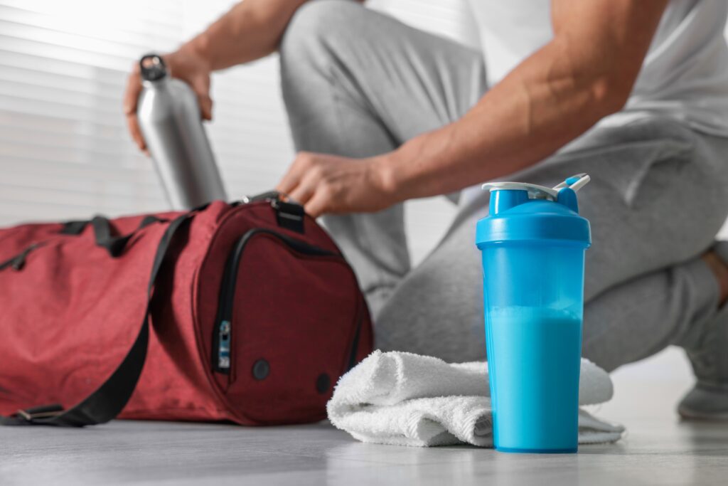 Un shaker de protéines est posé à côté d'un sportif préparant son sac de sport. 