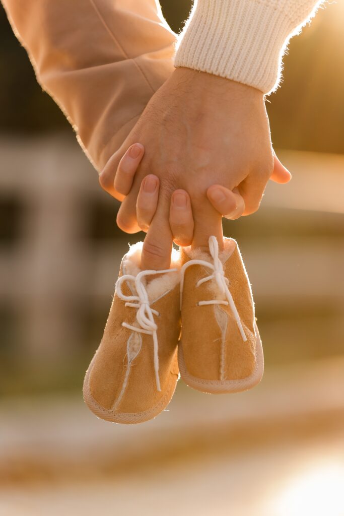 Deux mains entrelâcées, d'un homme et d'une femme, tiennent une paire de chaussures de bébé.
