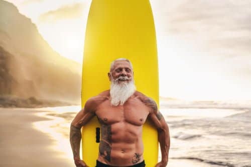 vieil homme musclé portant une planche de surf