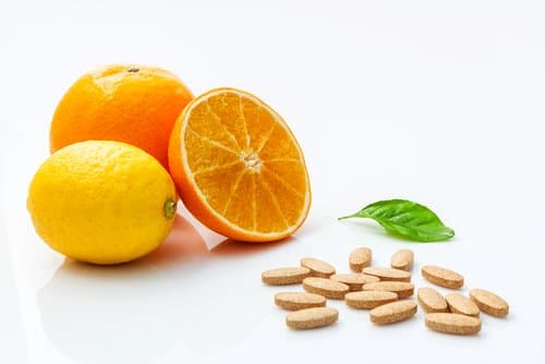comprimés de vitamine C à côté d'une orange coupée et d'un citron