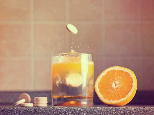 comprimés de vitamine C qui tombent dans un verre d'eau à côté d'une orange coupée en deux